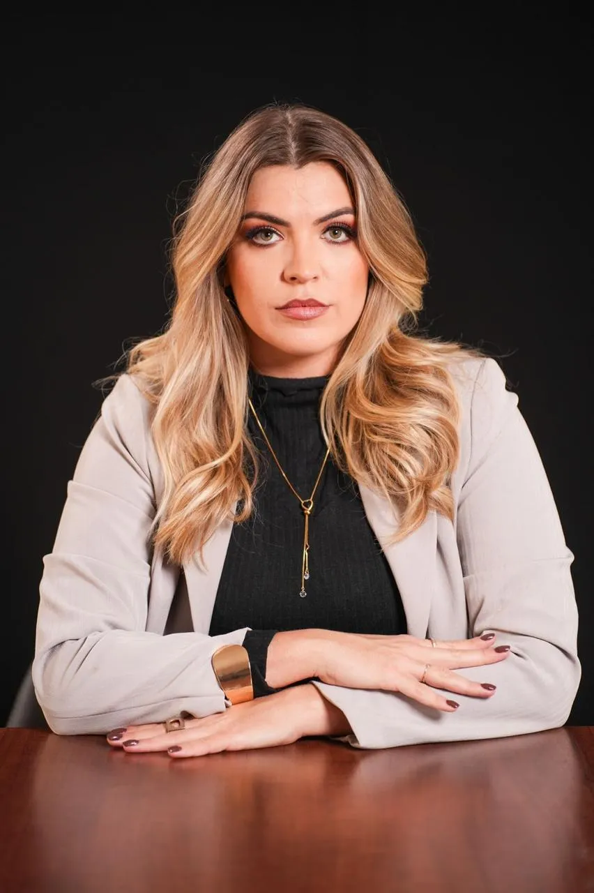 Advogada Laura Milléo sentada à mesa de trabalho, de blazer claro, com as mãos cruzadas